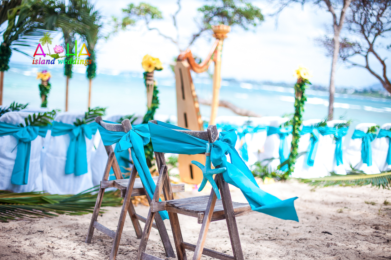 Beach setup with dark wooden chairs, turquoise sashes and a golden harp under the trees